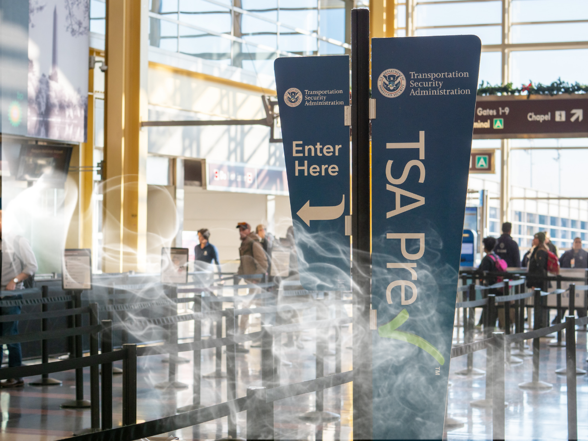 How To Travel With Cannabis Flower. Image showing TSA security checkpoint lines in an airport, with an overlay of smoke photoshopped over the image, portraying the idea of traveling with cannabis flower. 